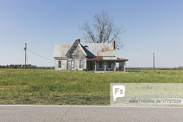 Verlassenes Haus mit rostigem Blechdach in einem Ackerland an einer Straße.