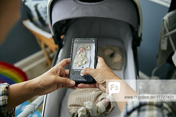 Mother taking photograph of 3 month old baby boy lying in baby buggy using smart phone