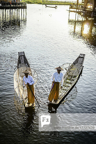 Two fishermen on traditional boats on the lake with fishing nets.