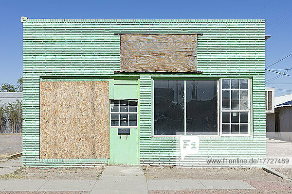 Verlassener Laden am Straßenrand in einer Kleinstadt  Fenster mit Brettern vernagelt  grün gestrichenes Äußeres.