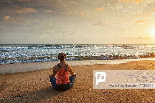 Frau macht Yoga  meditiert und entspannt in Padmasana Lotus Pose im Freien am tropischen Strand bei Sonnenuntergang
