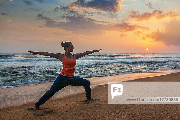 Frau macht Hatha Yoga Asana Virabhadrasana 1 Warrior Pose im Freien am Strand bei Sonnenuntergang. Kerala  Indien  Asien