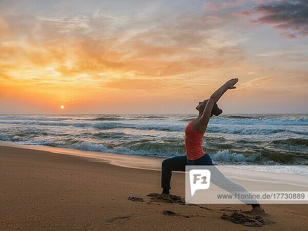 Woman doing Hatha yoga asana Virabhadrasana 1 Warrior Pose outdoors on ocean beach on sunset. Kerala  India  Asia