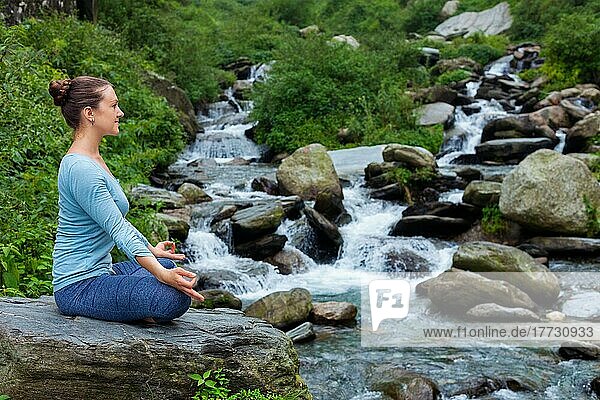 Frau in Hatha Yoga Asana Padmasana im Freien an einem tropischen Wasserfall