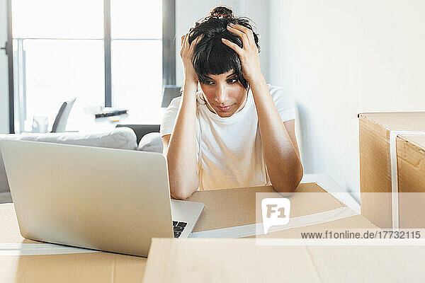 Frustrierte Frau schaut im neuen Zuhause auf Laptop