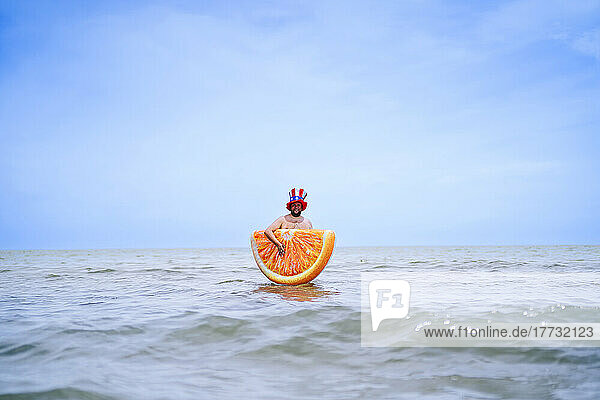 Man carrying inflatable orange slice standing in sea