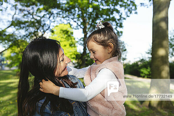 Smiling mother carrying daughter in park on sunny day