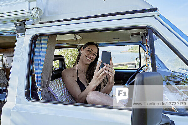 Happy woman on video call through smart phone in camper van