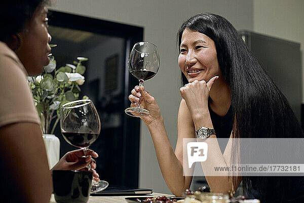 Happy woman holding wineglass talking to girlfriend at home