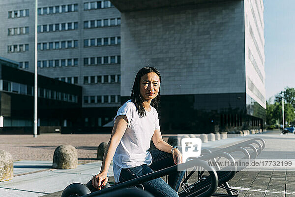 Geschäftsfrau sitzt an sonnigem Tag auf Fahrradständer