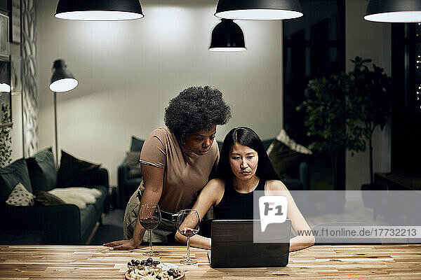 Woman using laptop by girlfriend standing at table