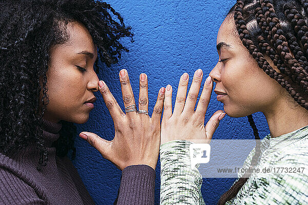 Frauen mit geschlossenen Augen gestikulieren vor einer blauen Wand