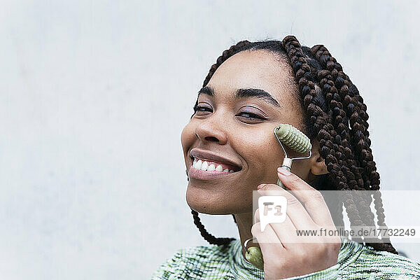 Smiling woman with jade roller against white background