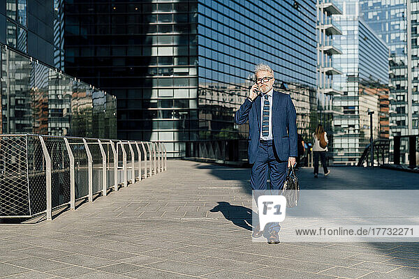 Senior businessman talking on smartphone walking outside office building
