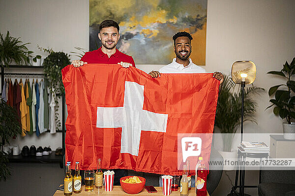 Happy football fans standing with Swiss flag at home