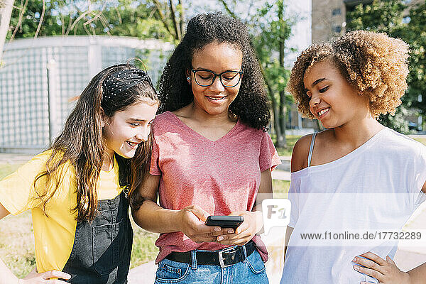 Happy young woman sharing smart phone with friends on sunny day