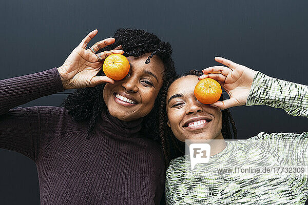 Fröhliche Freunde bedecken ihr Auge mit Orange vor der Wand