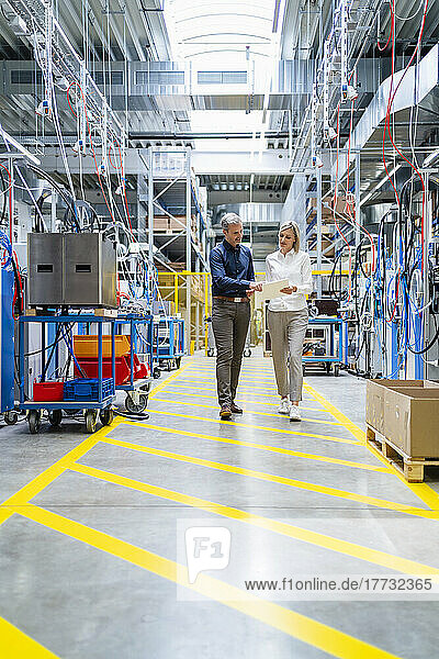 Businessman and businesswoman walking and talking in factory