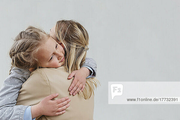 Tochter umarmt Mutter vor weißem Hintergrund