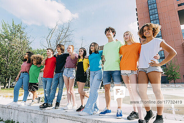 Smiling multiracial friends standing with arm around in front of building