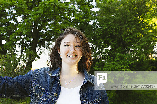 Smiling teenage girl wearing a denim jacket in front of bushes