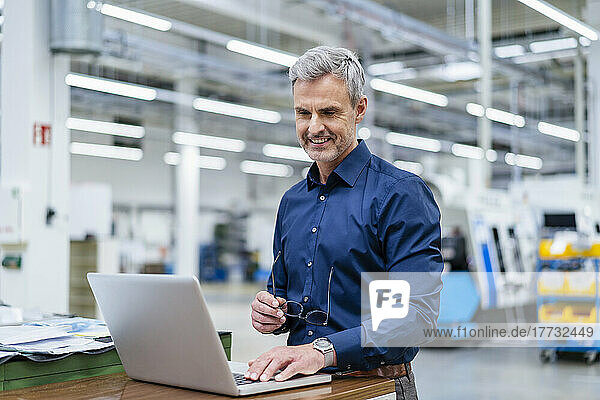 Mature businessman using laptop in factory
