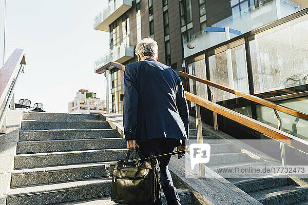 Senior businessman walking up steps outside office building on sunny day