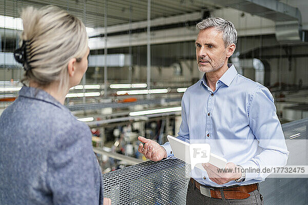 Businessman with digital tablet and businesswoman talking in factory
