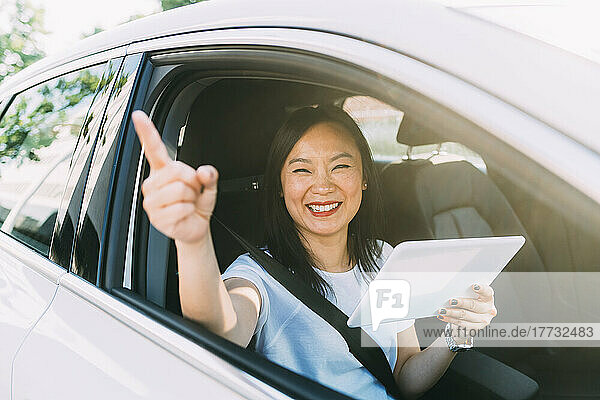 Glückliche Geschäftsfrau zeigt mit Tablet-PC im Auto auf Roadtrip