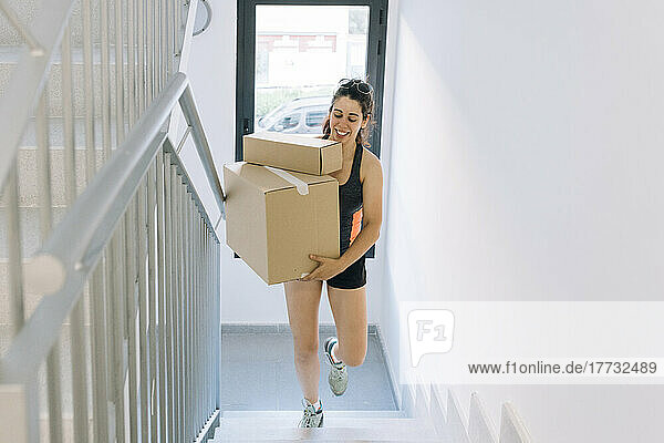 Smiling woman with cardboard boxes moving up on steps