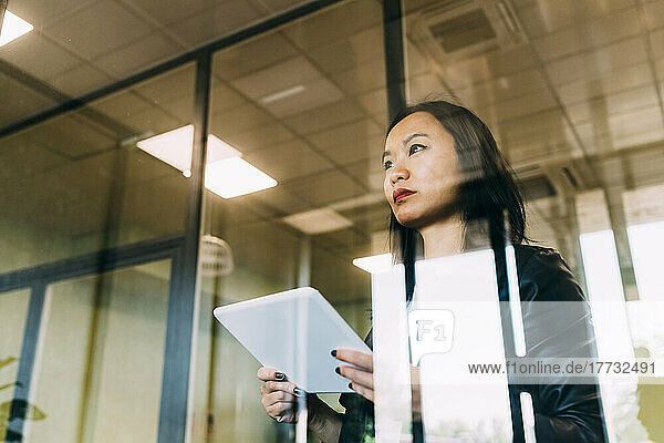 Confident businesswoman with tablet PC seen through glass at office