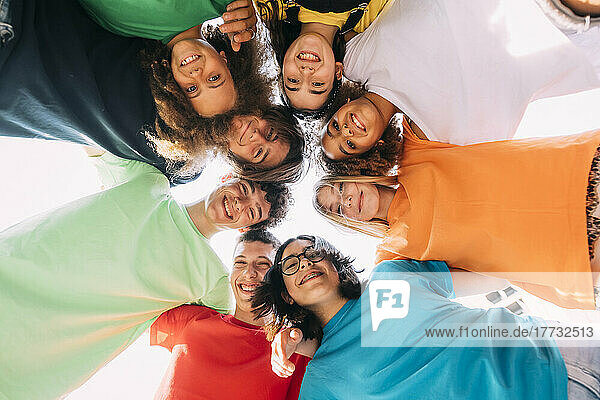 Happy multiracial friends huddling together on sunny day