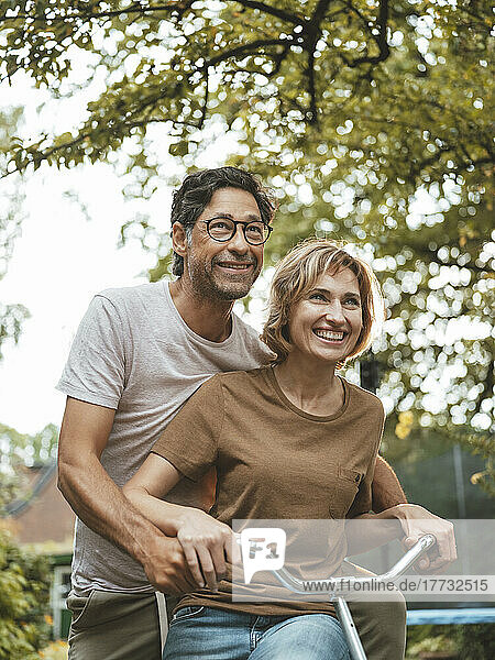 Happy mature man and woman riding bicycle together in back yard
