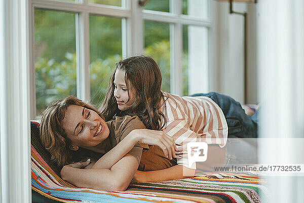 Smiling daughter with mother lying on sofa at home