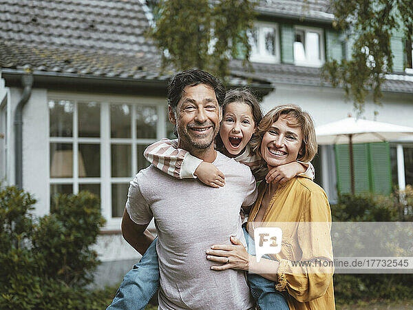 Happy mature parents with daughter standing in front of house