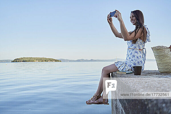 Lächelnde Frau fotografiert den See per Smartphone
