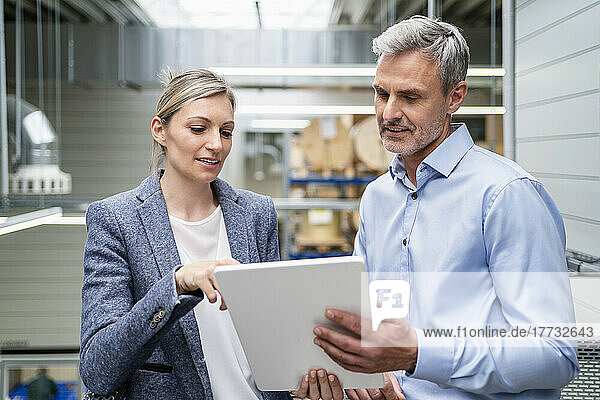 Businessman and businesswoman sharing digital tablet in factory