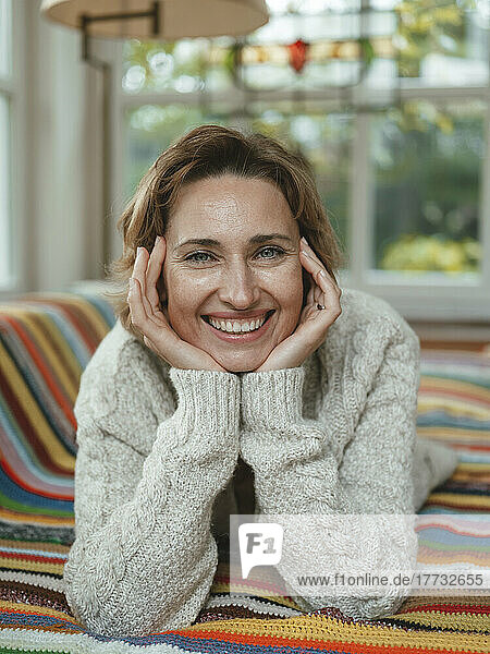 Happy mature woman wearing sweater lying on sofa at home