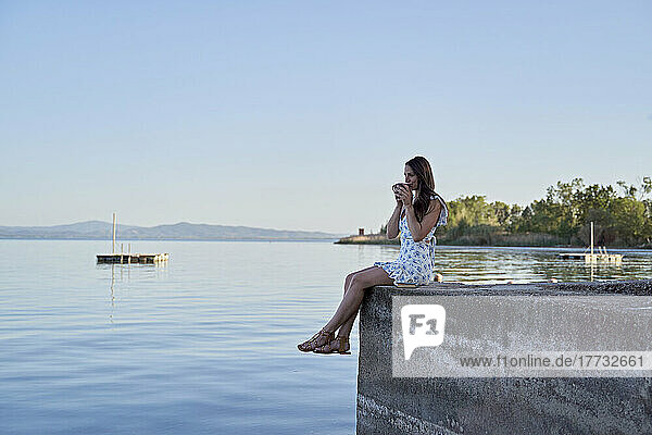 Frau trinkt Kaffee auf Steg am See