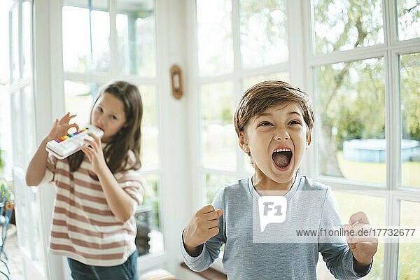 Boy screaming standing in front of sister playing musical instrument