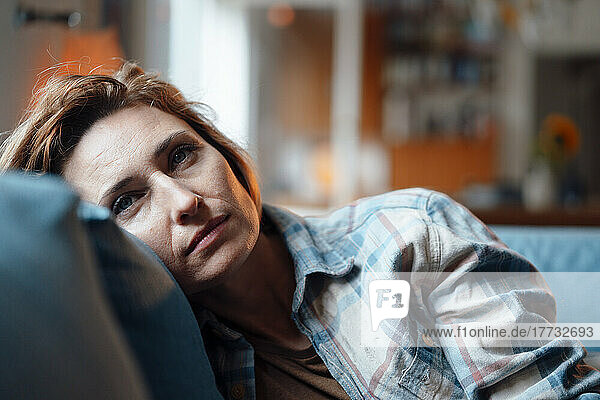 Thoughtful woman leaning on sofa in living room at home