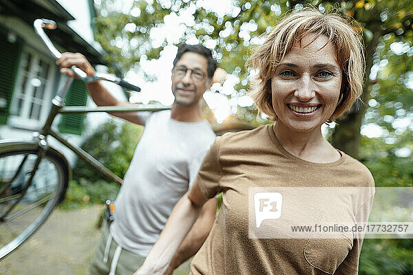 Happy mature woman with man carrying bicycle on shoulder in back yard