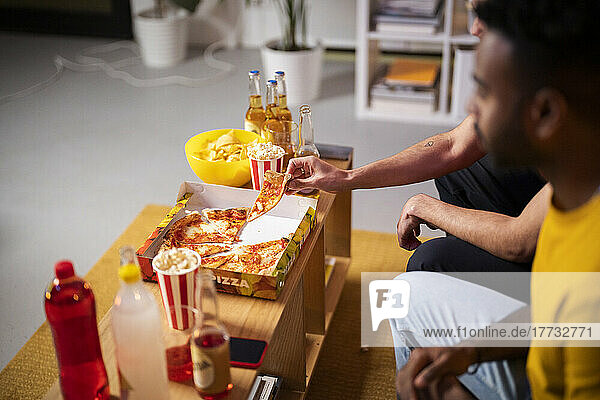 Hände eines jungen Mannes  der zu Hause von einem Freund ein Stück Pizza nimmt