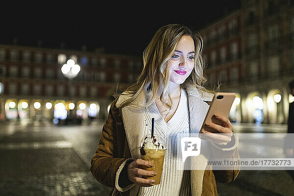 Frau mit Einwegbecher nutzt Smartphone in der Stadt