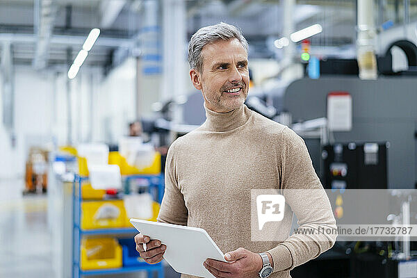 Smiling businessman holding digital tablet in factory