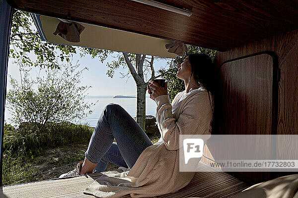 Woman having coffee in motor home by lake