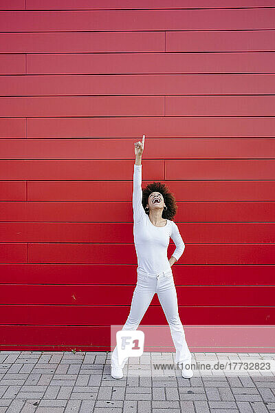 Cheerful young woman pointing up in front of red wall