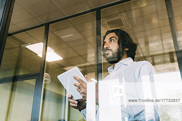 Confident businessman with tablet computer seen through glass at office