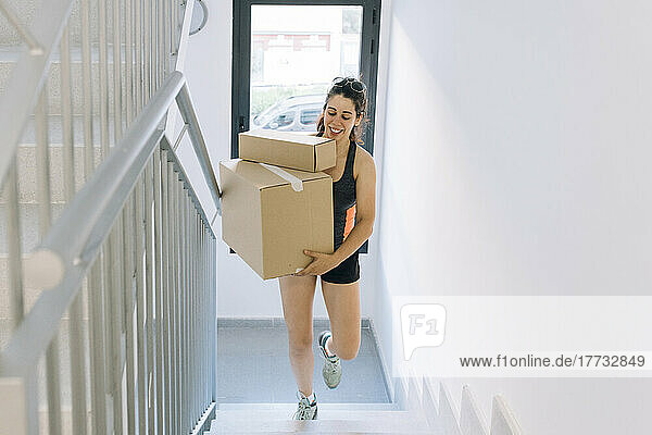 Happy woman carrying cardboard boxes moving up on steps