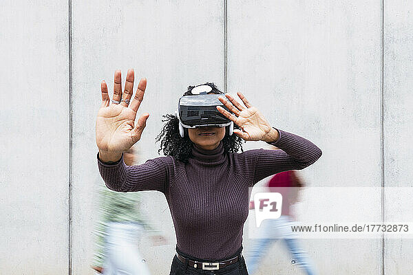 Woman wearing virtual reality simulator gesturing in front of wall